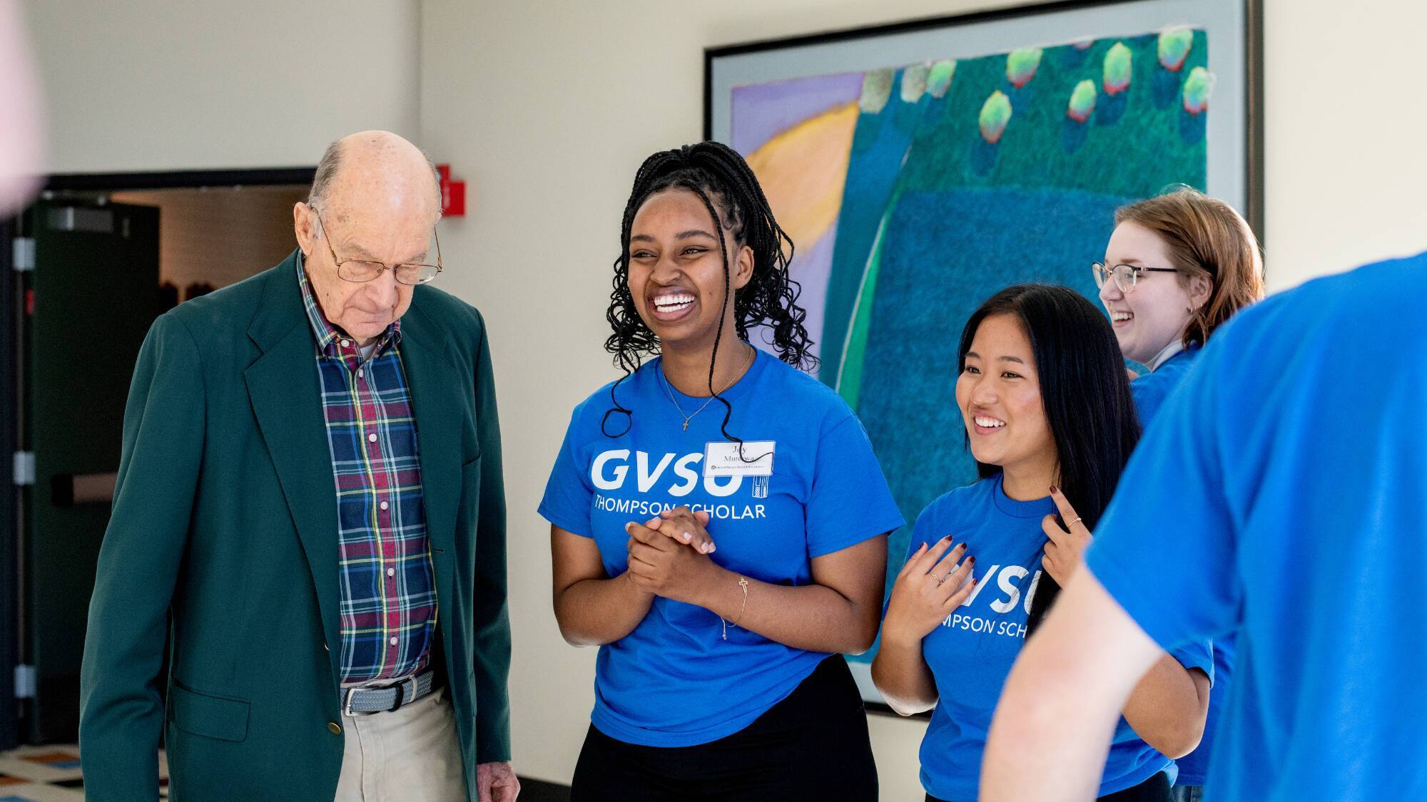Bob Thompson with three smiling students wearing blue Thompson Scholar t-shirts.